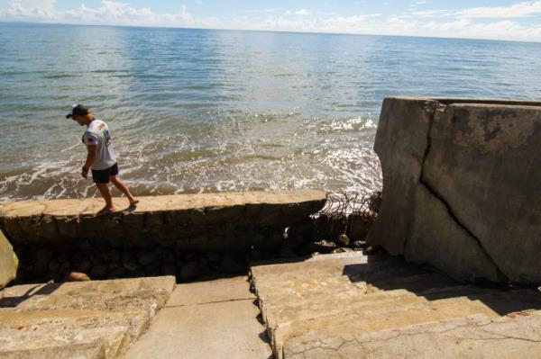 The government's sea wall. The co<em></em>ncrete is crumbling. Someone is standing on top of it. The sea is behind.