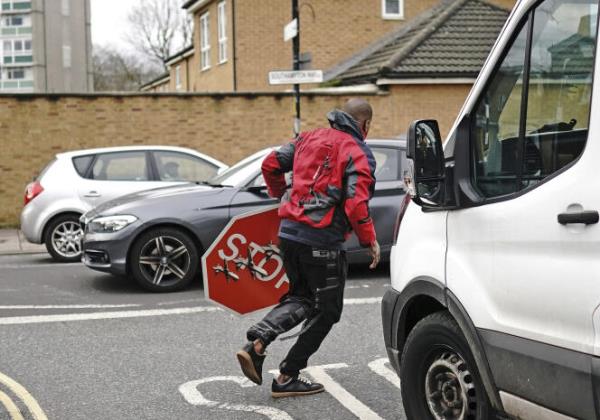 A person removes a piece of art work by Banksy, which shows what looks like three dro<em></em>nes on a traffic stop sign, which was unveiled at the intersection of Southampton Way and Commercial Way in Peckham, southeast London, Friday December 22, 2023.