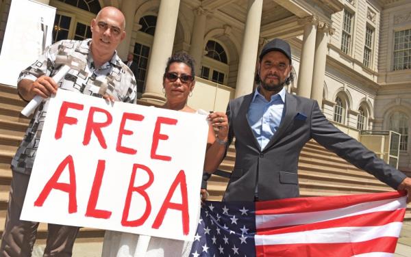 Protesters holding signs and a flag on the steps of City Hall supporting Jose Alba