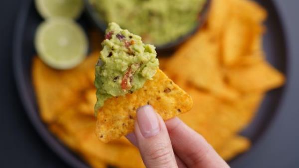 Closeup of woman hand holding guacamole and chips or nachos. Top view