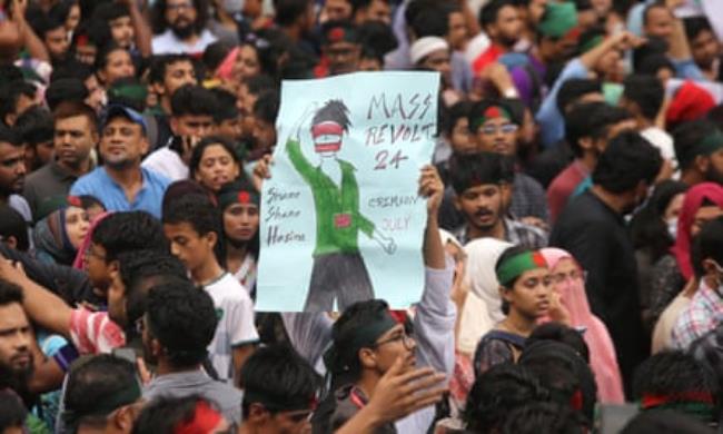 A crowd of young South Asian people, many wearing headbands in the colours of Bangladesh's flag. One holds a placard saying 'Mass revolt 24"