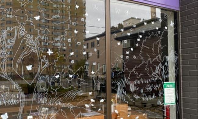 A window with the outline of trees, grass and butterflies drawn on it in white chalk marker.