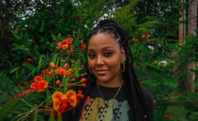 A woman stands outside next to bright orange and red flowers.