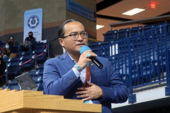 man wearing suit and glasses speaks into microphone