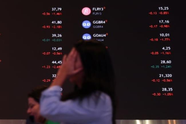 A person walks by an electro<em></em>nic board displaying information of recent fluctuations of market indices at the B3 Stock Exchange in São Paulo.