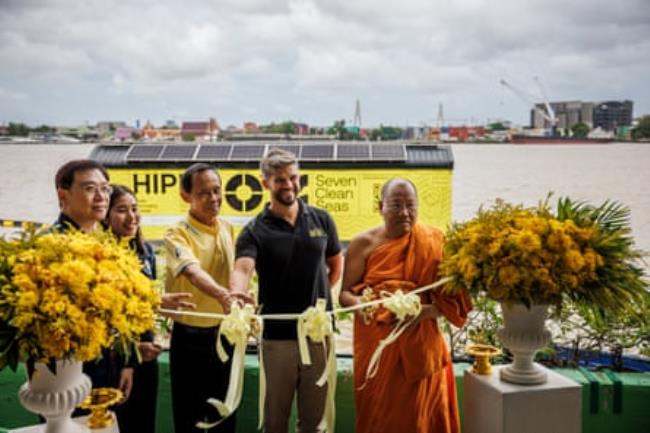 A Thai monk, three other Thais and a western man cut a ribbon with a yellow Hippo boat on the Chao Phraya River, Bangkok, in the background.