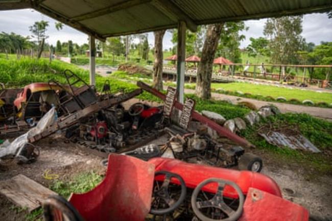 Abando<em></em>ned and broken up go-karts rusting away in an open shed with a race track beyond.