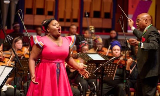 An African soloist singing in front of an Orchestra in a co<em></em>ncert hall