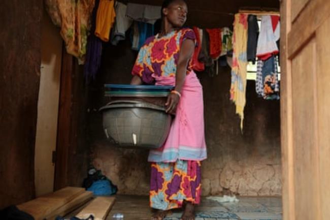 A woman in a colourful dress stands alo<em></em>ngside washing that has been hung out to dry, holding a stack of plastic buckets