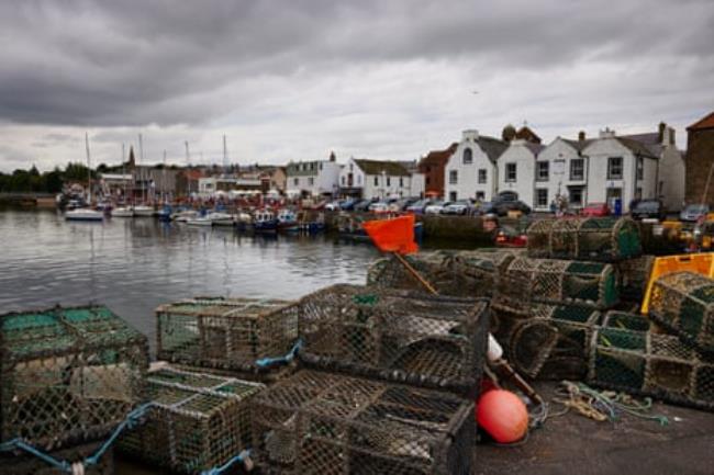 Crab and lobster pots stacked on a quay with small fishing boats in the background