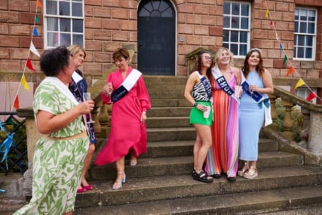 Six women of various ages in bright dresses and wearing sashes hold champagne glasses and pose for photos