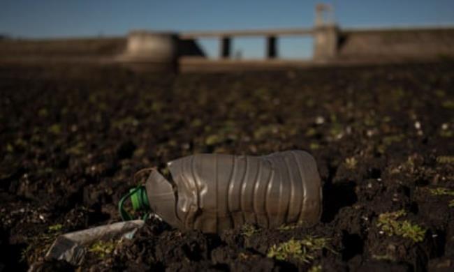 A plastic bottle lying on dried-up soil with a dam in the background