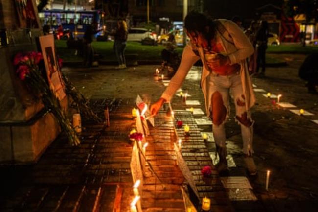 A trans woman lights one of many candles on the street alo<em></em>ngside photographs at night