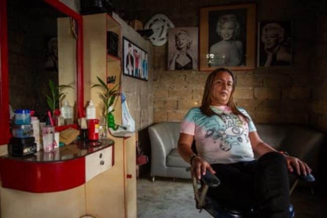 A trans woman sits in a chair next to some hairdressing tools