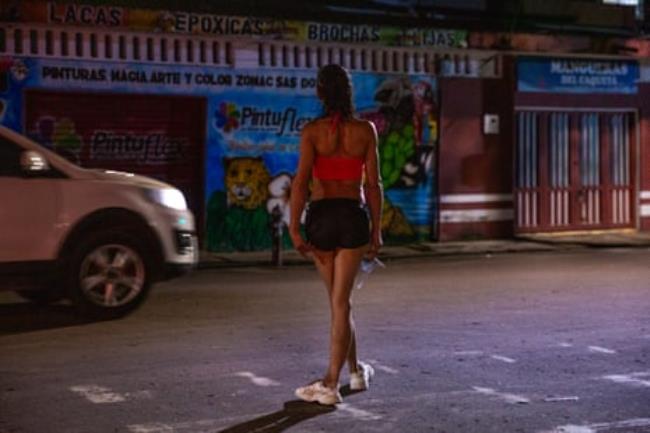 A trans woman stands on a street at night