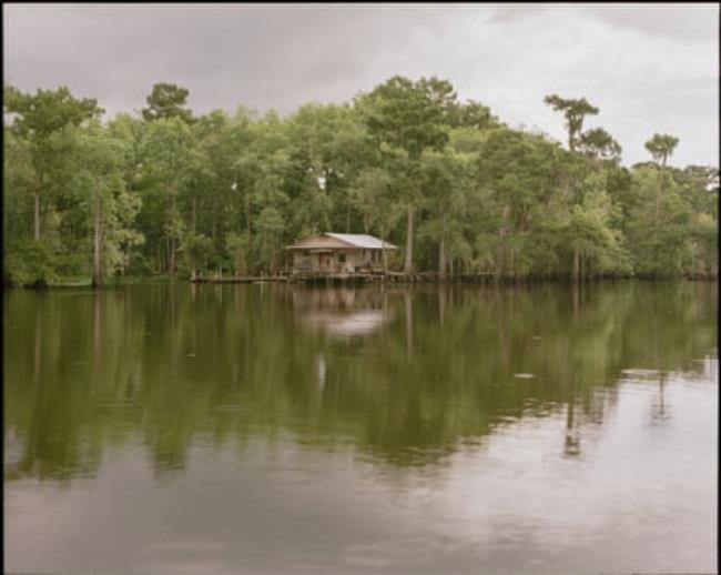 A lake surrounded by vegetation with a structure in on the distant shore.