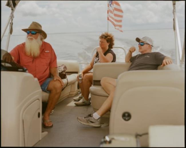 Three middle-aged people enjoy a boat ride with a US flag flapping behind them.