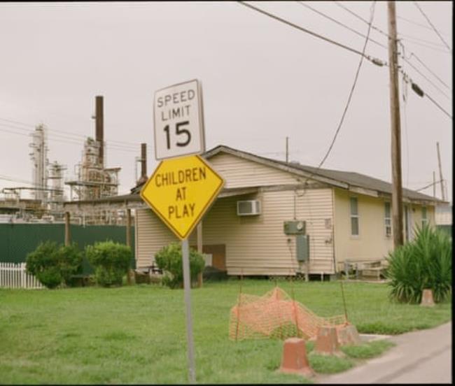 A home sits near an industrial facility with a ‘Children at Play’ sign nearby.