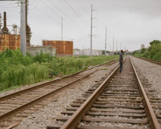 A man walks on train tracks next to an industrial facility.