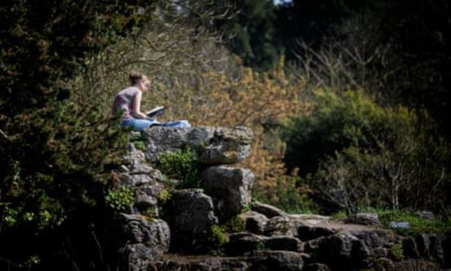 A woman reads a book on rocks in a park