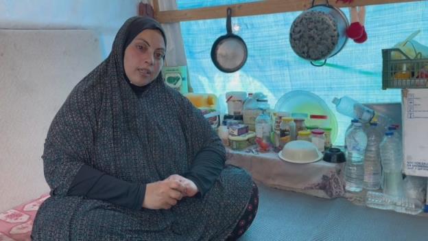 A woman sits in a tent surrounded by pots, pans and tupperware. 