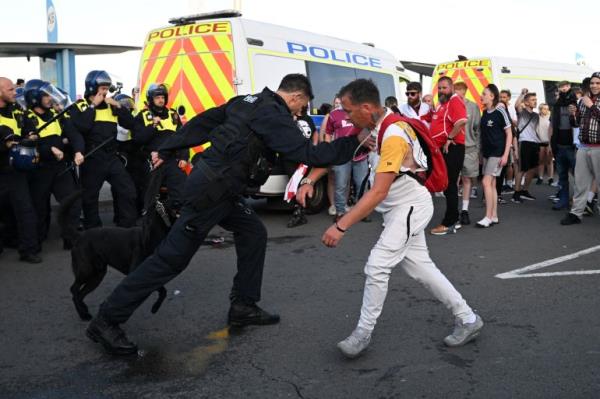 A protester co<em></em>nfronts a policeman with a dog. There are police officers lined up one side and a crowd of men on the other. A police van is behind