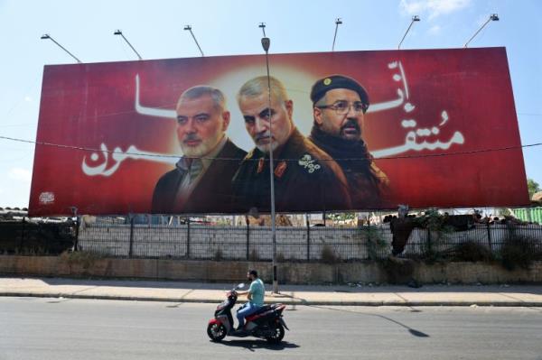 TOPSHOT - A man rides his moped past a billboard bearing portraits of slain leaders, Ismail Haniyeh of the Palestinian militant group Hamas, Iranian Quds Force chief Qasem Soleimani (C), and Hezbollah senior commander Fuad Shukr on the main road near the Beirut Internatio<em></em>nal Airport on August 3, 2024. (Photo by Ibrahim AMRO / AFP)