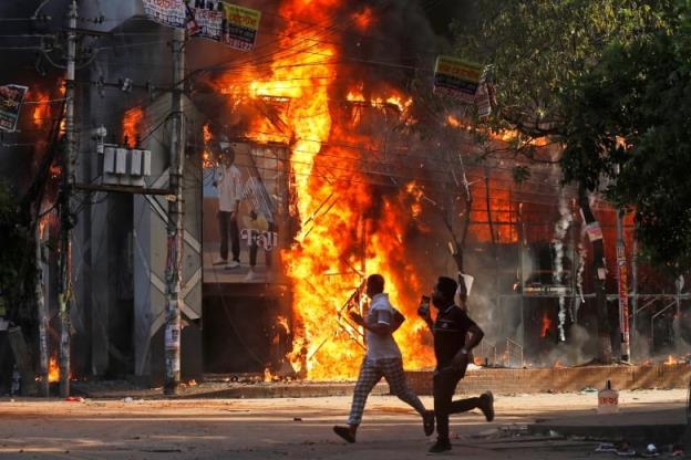 Two people run in front of a burning building.