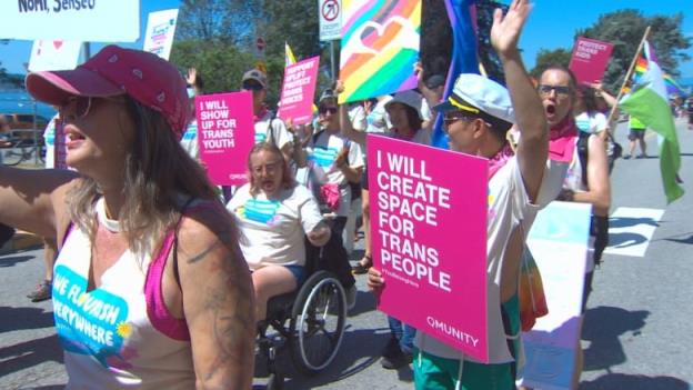 Bunch of people at a parade wearing colorful clothes and holding banners