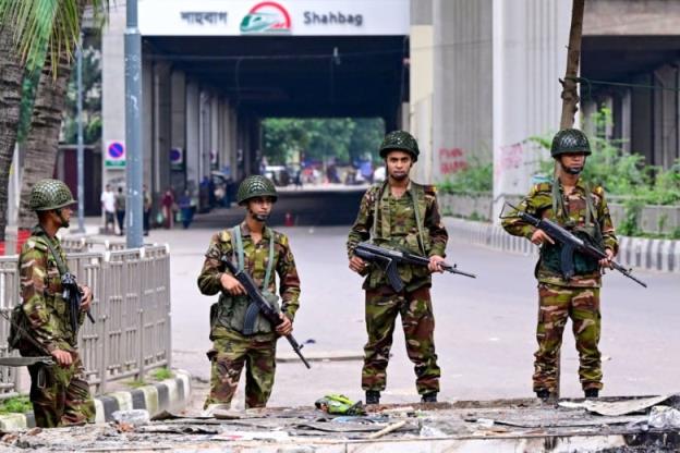 Soldiers holding guns stand guard on the street.