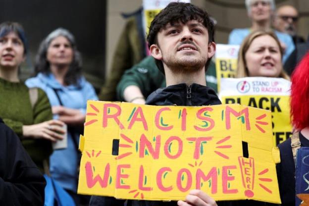 A person holds a sign that reads, 'Racism not welcome here,' during a demonstration.