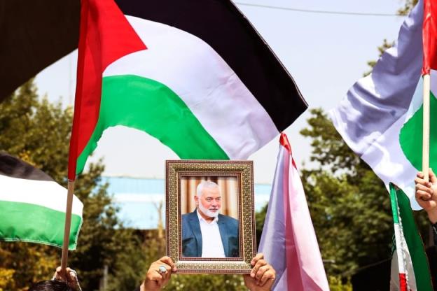 A person holds a f<em></em>ramed photo of a bearded man near waving Palestinian flags.