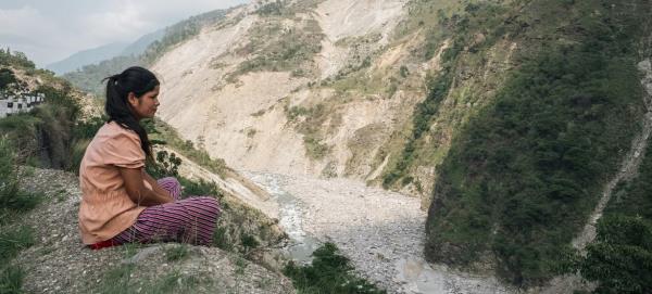 In western Nepal, a girl sits on the edge of a cliff, overlooking a massive landslide brought on by the mo<em></em>nsoon rains in 2023.