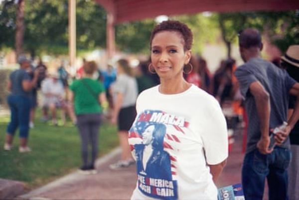 a woman smiles while wearing a shirt that reads ‘Kamala make America laugh again’