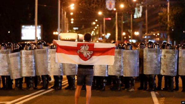 FILE - A protester holds an old Belarusian natio<em></em>nal flag as he stands in front of police line during a rally after the Belarusian presidential election in Minsk, Belarus, Aug. 9, 2020.