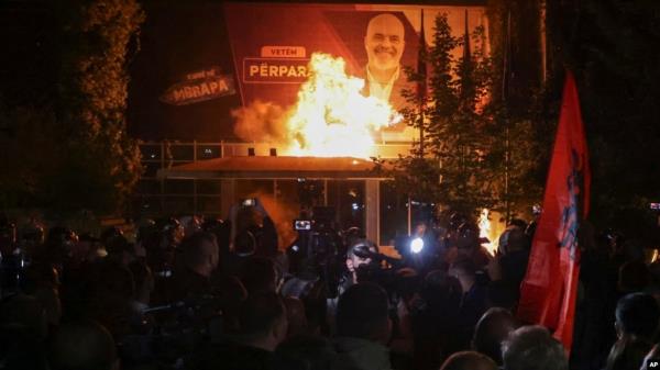 Fire burns behind a riot police cordon and in front of a poster depicting the Albania Prime minister Edi Rama during an anti-government rally set up by the opposition, in Tirana, Albania, Monday, Oct. 7, 2024. 