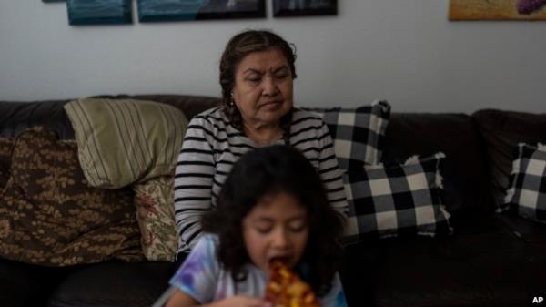 Marina Maalouf, a lo<em></em>ngtime resident of Hillside Villa, sits on a sofa as her granddaughter eats pizza for lunch in their apartment in Los Angeles, Oct. 1, 2024.