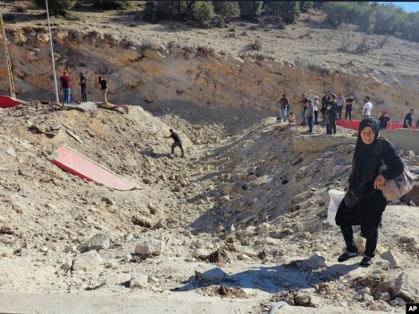 A woman carries her belo<em></em>ngings crossing on foot into Syria through a crater caused by an Israeli airstrike to cut the road between the Lebanese and the Syrian checkpoints, at the Masnaa crossing, in the eastern Bekaa Valley, Lebanon, Oct. 4, 2024.