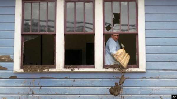 Ben Phillips scoops mud out a window of his house left in the wake of Hurricane Helene, in Marshall, North Carolina, Oct. 1, 2024.