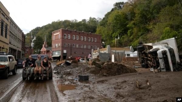 People ride in the back of a pickup truck on a mud-covered street left in the aftermath of Hurricane Helene, in Marshall, North Carolina, Oct. 1, 2024.