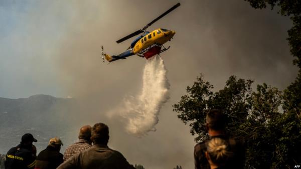 A firefighting helicopter drops water drop as a wildfire burns in the village of Pyrgos, near Corinth, Greece, on September 30, 2024.