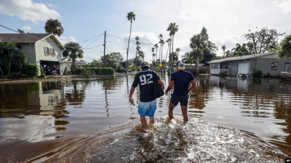 Thomas Chaves, left, and Vinny Almeida walk through floodwaters from Hurricane Helene in an attempt to reach Chaves's mother's house in St. Petersburg, Florida, Sept. 27, 2024.