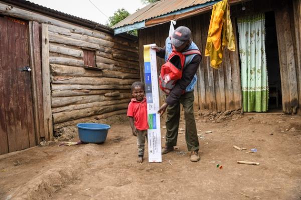 Pascal, a Community Drug Distributor (CDD), measures three-year-old Praygod's height to determine the correct dose of azithromycin syrup during a Mass Drug Administration (MDA) in Kajaido, near the Kenyan-Tanzania border. Credit: Sightsavers/Samuel Otieno