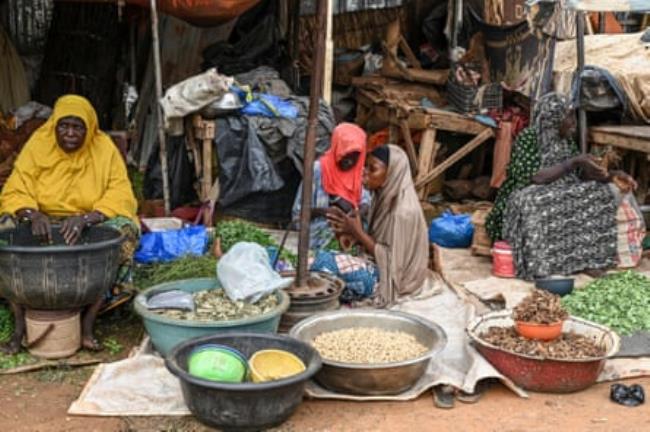 African women in colourful abayas sitting behind bowls of pulses and vegetables in front of a stall 