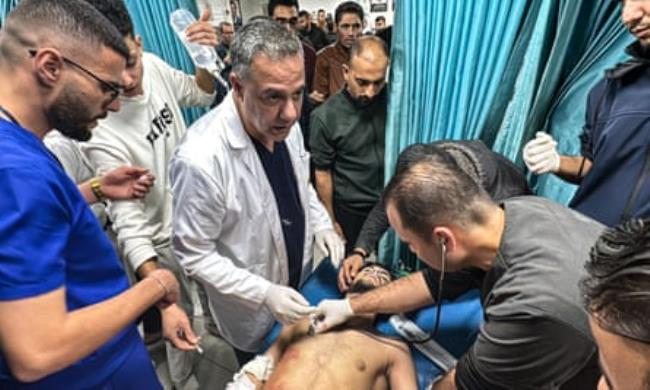 A doctor in a white coat talking to other medics as a man lies on a gurney